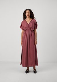Robe maxi dans une couleur rose atténuée, fabriquée en tissu texturé avec un décolleté en V, des manches courtes et une taille froncée ; présente des fentes sur les côtés.