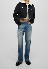 Veste courte en denim noir avec col en sherpa, associée à un jean large bleu clair avec un léger délavage et des bottes noires.