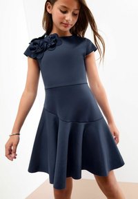 Rochie bleumarin cu mâneci scurte, corset ajustat și fustă evazată. Prezintă flori din material pe un umăr. Textură netedă, design simplu.