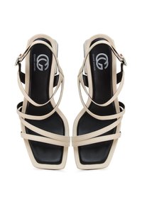 Sandales à talons hauts beiges avec des brides, dotées d'un design à bout carré, présentant une semelle intérieure noire et des brides de couleur claire avec des détails subtils.