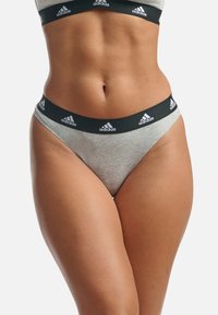 Graue Baumwoll-Strings mit einem schwarzen Bund, der mit weißen Adidas-Logos und einem minimalistischen Design versehen ist. Glatte Textur und dehnbare Passform.