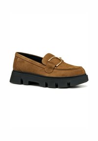 Bruine suède loafers met een gouden gesp en een zwarte dikke gekartelde zool. De schoen heeft een ronde neus en gestikte details op de bovenkant.
