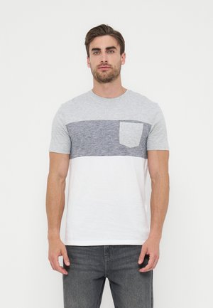 Άνδρας φοράει κοντομάνικο t-shirt με χρωματικό μπλοκ, με ριγέ γκρι πίνακα στο στήθος και μικρό τσεπάκι, συνδυασμένο με σκούρο γκρι τζιν.