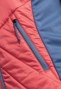 Isolierte Jacke mit diagonaler Steppung in Koralle und einem einfarbigen blauen Einsatz. Ausgestattet mit einem navyfarbenen Reißverschluss mit Zugband.