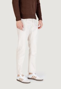 Jeans in denim bianco con taglio dritto, indossati con un maglione lavorato a maglia marrone e sneakers bianche con strisce marroni. Design semplice e vestibilità comoda.