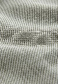 Približen posnetek bež in bele teksturirane tkanine z rahlim vzorcem ribje kosti in nežnimi pregibi.