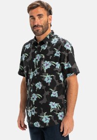 Cămașă cu mânecă scurtă, cu nasturi, de culoare neagră, cu un model floral în nuanțe de albastru și verde. Prezintă un buzunar pe piept și un design relaxat.