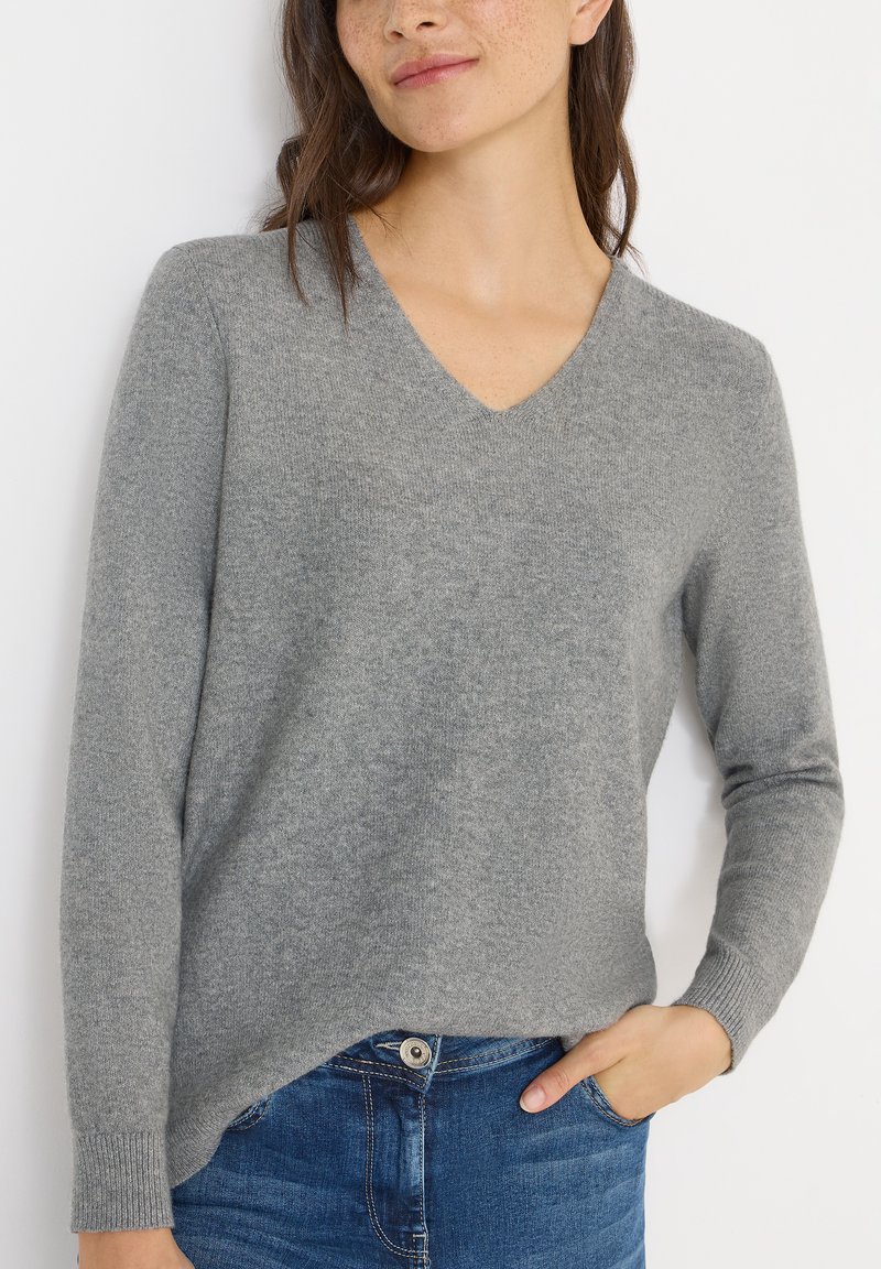 Grauer V-Ausschnitt-Pullover aus weichem Strickstoff, mit langen Ärmeln und lockerer Passform, kombiniert mit blauen Jeans.