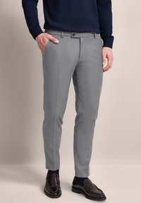 Grau maßgeschneiderte Hose mit slim Fit, flachem Vorderteil und zwei Seitentaschen, kombiniert mit dunklen Slippern und einem marineblauen Pullover.
