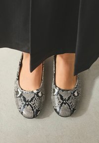 Flade sko med et sort og hvidt slangeprintmønster, rundet tå, glat tekstur, sat mod en neutral overflade.