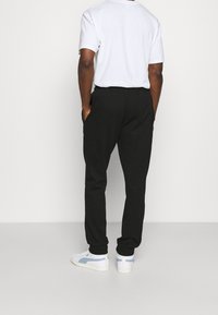 Black sweatpants with elastic cuffs, a drawstring waistband, and side pockets, paired with a white short-sleeve t-shirt and white sneakers.