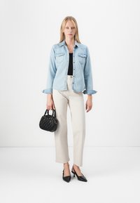 Light blue denim jacket with two chest pockets, black top, cream trousers, black textured handbag, and pointed black heels.