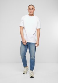 Valge puuvillane T-särk lühikeste varrukatega, koos helesiniste denim teksadega. Kantud beeži ja valge sportjalatsitega. Lihtne, kaugelt casual disain.