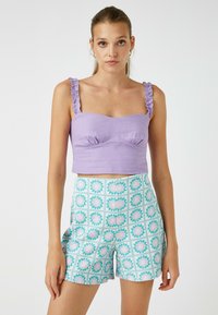 Top corto lilla con spalline arricciate e design aderente, abbinato a pantaloni shorts leggeri blu chiaro con motivi floreali e una griglia quadrata.