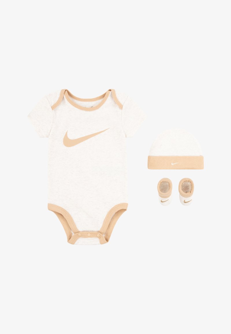 Το σετ ρούχων για μωρό περιλαμβάνει ένα κορμάκι με κοντά μανίκια σε κρεμ χρώμα με μπεζ λεπτομέρειες, ένα ταιριαστό καπέλο και παπουτσάκια, όλα με το λογότυπο της Nike.
