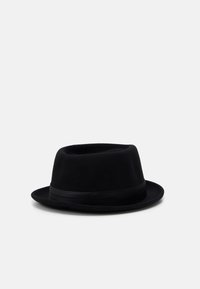 Chapeau en feutre noir avec une couronne courte et arrondie et un large bord. Présente un bandeau en satin noir autour de la base de la couronne. Texture lisse.