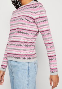 Pull à manches longues en gris clair avec un motif géométrique en rose et noir. Encolure ras du cou, poignets et ourlet côtelés, texture douce.