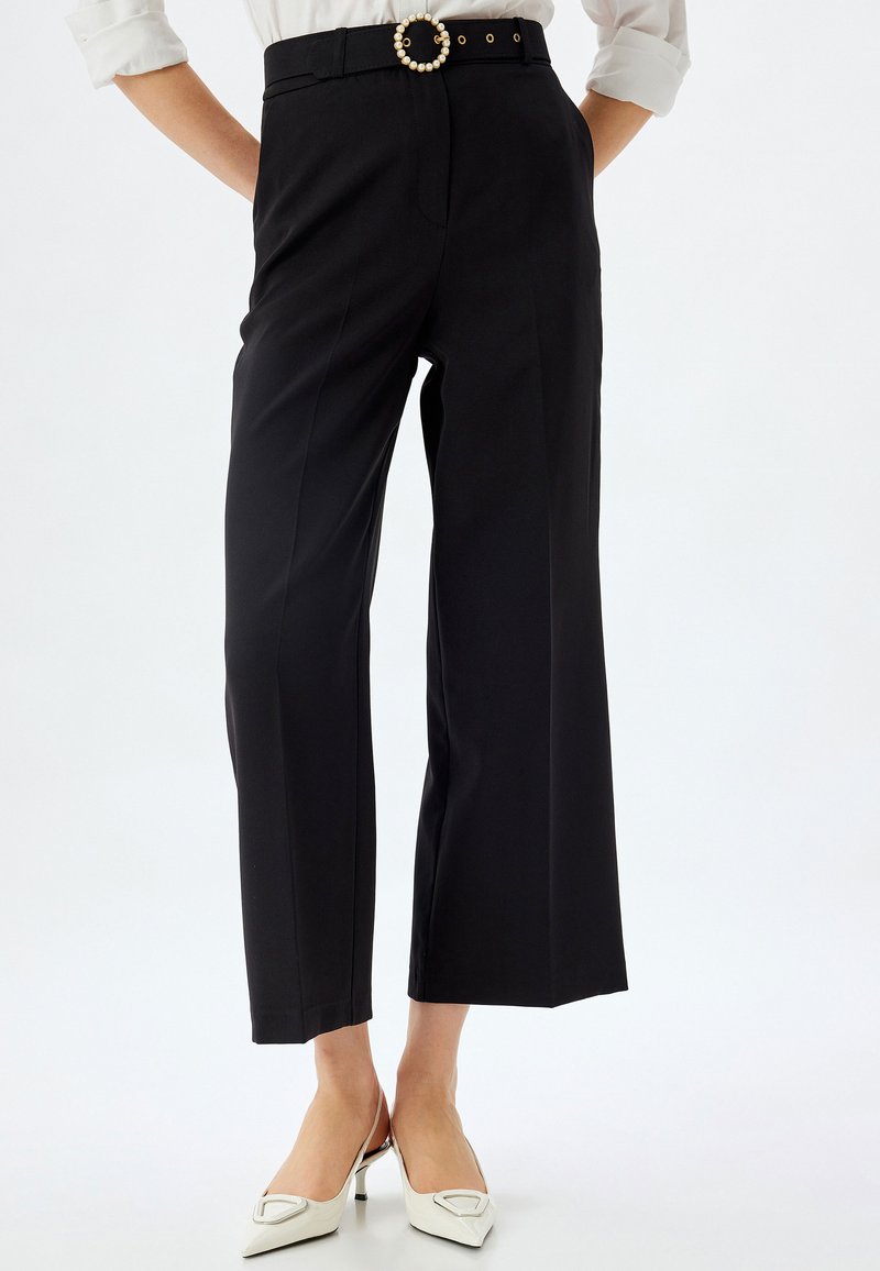 Schwarze Hose mit maßgeschneidertem Design, weitem Bein und einem Gürtel mit einer runden Perlenakzent. Glattes Material mit minimaler Textur.