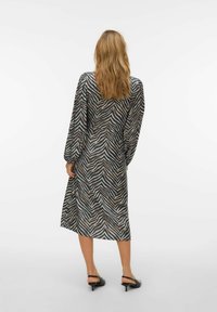 Garām piedurknēm, ceļgalu garuma kleita ar melnu un bēšu zebras rakstu, ar brīvu piegriezumu un vieglu spīdumu, kopā ar melnām augstpapēžu kurpēm.