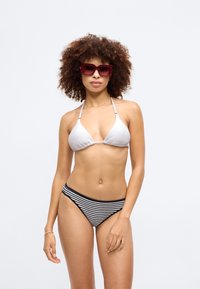 Bikini-set med en teksturert hvit trekantet topp og høy midje svartstripet bunn; modellen har på seg store røde solbriller.