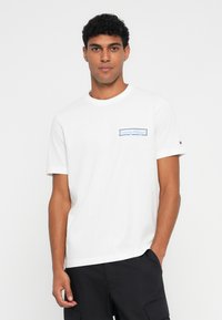 Hvit bomulls t-skjorte med en blå "Tommy Hilfiger"-logo på venstre bryst, rund hals og korte ermer.