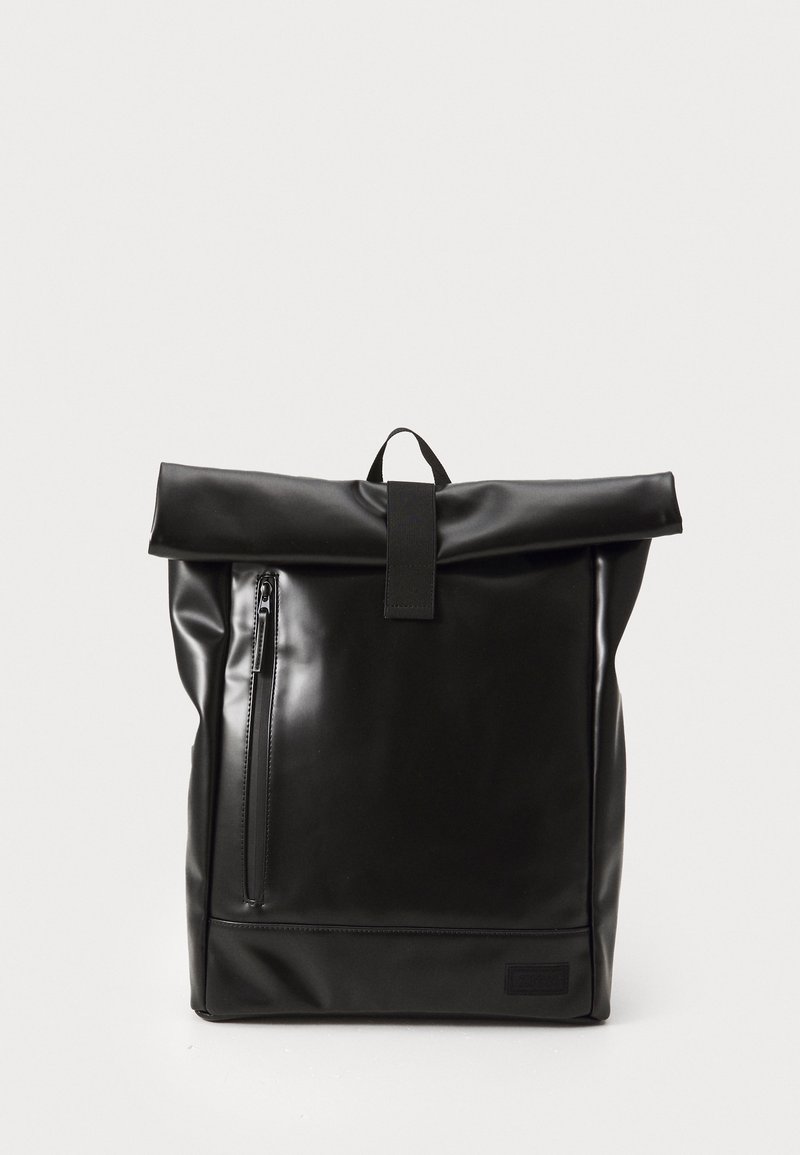 Sac à dos noir à fermeture roulante, avec poche zippée verticale à l'avant et poignée de transport supérieure sur fond clair uni.