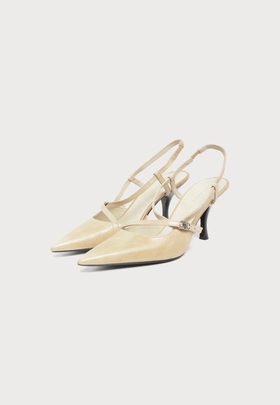 Escarpins slingback beige à bout pointu avec fines brides et petits talons noirs incurvés sur un fond uni.