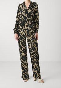 Combinaison à manches longues en beige avec des rayures de tigre noires. Comprend un col, une fermeture à boutons et une taille ceinturée. Le tissu semble doux et léger.