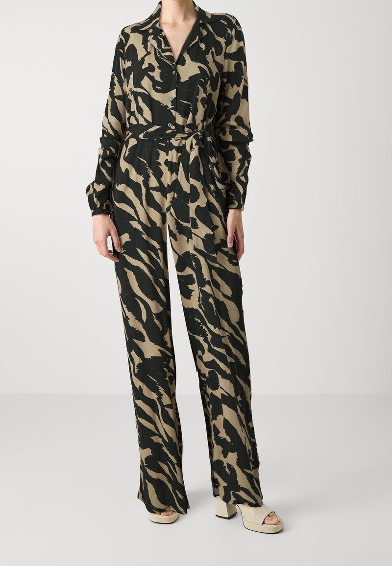 Combinaison à manches longues en beige avec des rayures de tigre noires. Comprend un col, une fermeture à boutons et une taille ceinturée. Le tissu semble doux et léger.