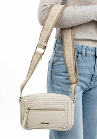 Beige læder crossbody taske med en struktureret overflade, justerbar rem med et geometrisk mønster og en frontlomme med lynlås.