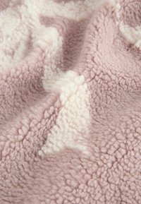Pehmeä fleece-peite, jossa on teksturoitu, ylellinen pinta vaaleanpunaisena ja kermanvärisin tehostein, esittäen hienovaraista kuviota.
