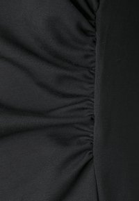 Melna auduma apdare ar teksturētu, krunkotu dizainu vienā pusē, gluda otrā pusē, demonstrējot mīkstu, elastīgu materiālu.