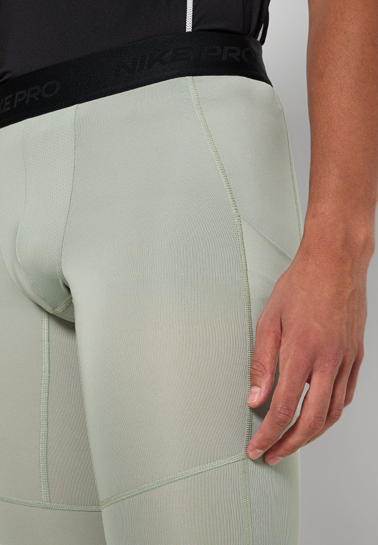 Acercamiento de una persona que lleva leggings de compresión verde claro con una cinturilla elástica negra y la mano descansando sobre el muslo.