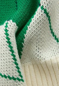 Pletena majica s teksturiranom bijelom podlogom i zelenim geometrijskim uzorcima, s rebrastim rubom i mekanim, toplim materijalom.