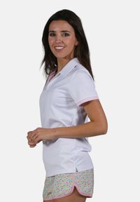 Polo blanc avec des accents roses au niveau du col et des manches, associé à un short à motif floral coloré avec une bordure rose.