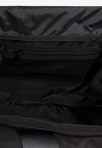 Interior de bolsa de tela negra con un bolsillo con cremallera. Presenta una textura suave y costuras reforzadas. Diseño ligero y espacioso.