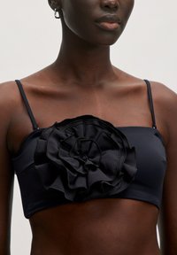 Zwarte bandeau top met dunne bandjes en een grote geraffineerde bloemenmotief aan de voorkant. Glad materiaal met een aansluitend ontwerp.