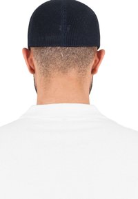 Fekete hálós sapka rövid hajon, hátulról nézve. Fehér pólóing gallérja látható. A haj világosbarna és rövidre nyírt.