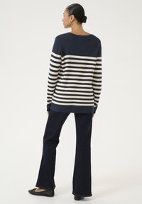 Jūras spēku un krēmkrāsas svītrainais džemperis ar brīvu piegriezumu, ar garām piedurknēm un platām malām. Savai izskatam pievienoti tumši plati džinsi un melnas dzīvokļu kurpes.