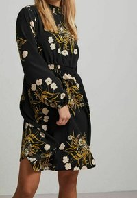 Abito nero floreale con maniche lunghe, caratterizzato da una vita cintrata, motivi floreali bianchi e gialli, e una vestibilità morbida. Tessuto dal texture liscia.