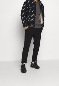 Black denim jacket with white "OBEY" print, gray t-shirt, black pants, and black sneakers. The jacket has a faux shearling lining.