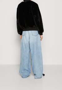 Sort faux fur bomberjakke med ribbet talje, parret med lyseblå vidde denim bukser. Bagfra viser den oversized pasform.