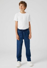 Tricou alb din bumbac combinat cu pantaloni din denim albastru, prevăzuți cu talie elastică și șnur. Model purtând adidași albi.