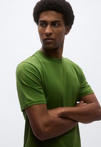 Πράσινο κοντομάνικο μπλουζάκι από βαμβάκι. Απλή σχεδίαση με στρογγυλή λαιμόκοψη και εφαρμοστή γραμμή, με ένα μικρό λογότυπο στο στήθος.