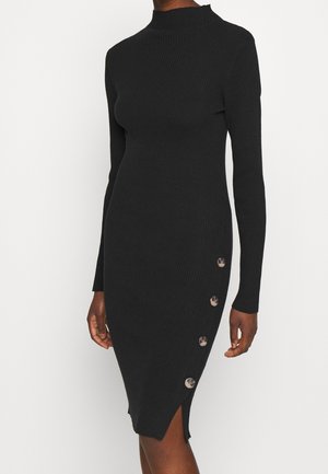 Czarna, długorękawowa sukienka z prążkowanego dzianiny z półgolfem i czterema dużymi guzikami po boku, noszona przez osobę na jednolitym jasnym tle.