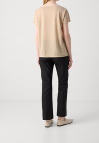 Camisa beige de manga corta con un corte relajado, combinada con pantalones negros, que presentan un diseño sencillo y una textura suave. Unos zapatos planos beige completan el conjunto.