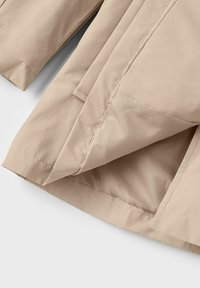 Tissu beige avec des détails de couture précis, montrant des couches superposées pliées et des bords ourlés sur une surface textile lisse.