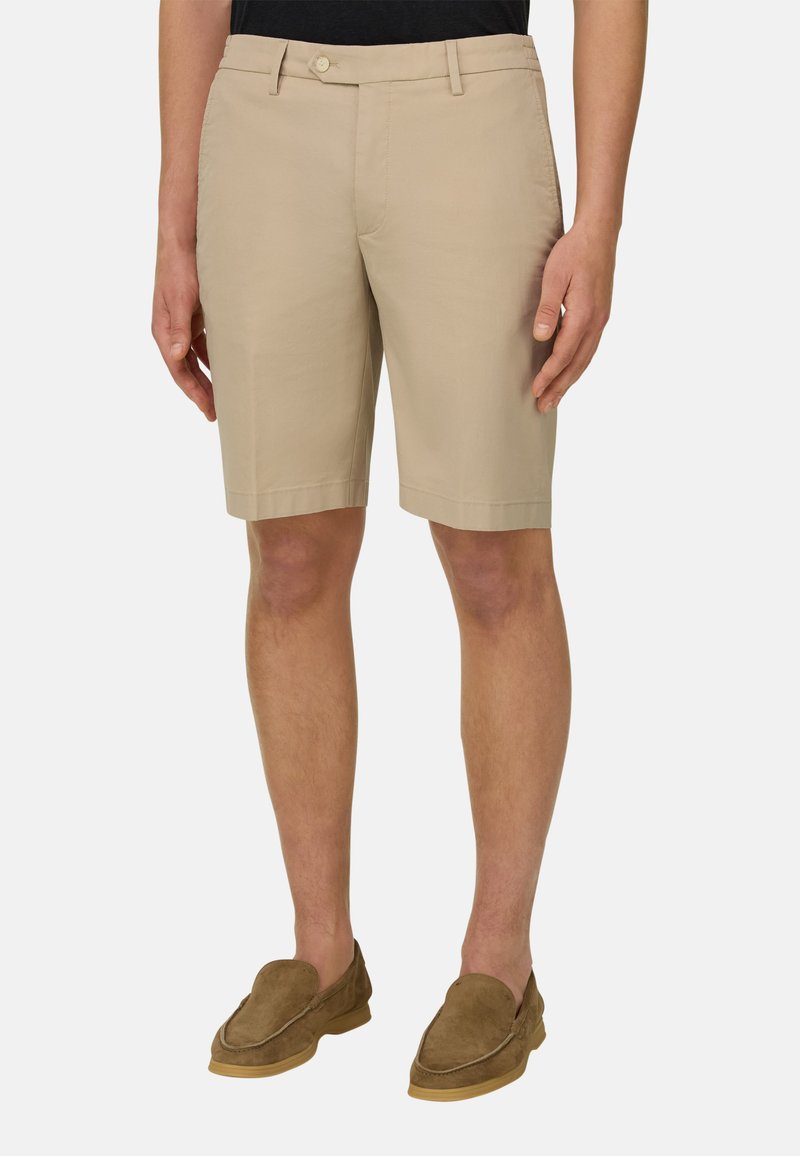 Short beige longueur genou avec passants de ceinture porté par une personne debout, associé à des mocassins en daim marron et un haut noir.