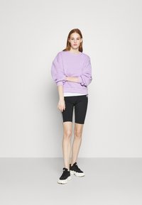 Lavender oversized sweatshirt met een gebogen halslijn, gecombineerd met zwarte fietsbroek met witte zijkanten, en zwarte sportieve schoenen.