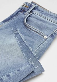 Vaaleansiniset farkut, joissa on revitty helma, hopeinen nappi ja kontrastivärinen keltainen tikkaus. Klassinen viiden taskun muotoilu.